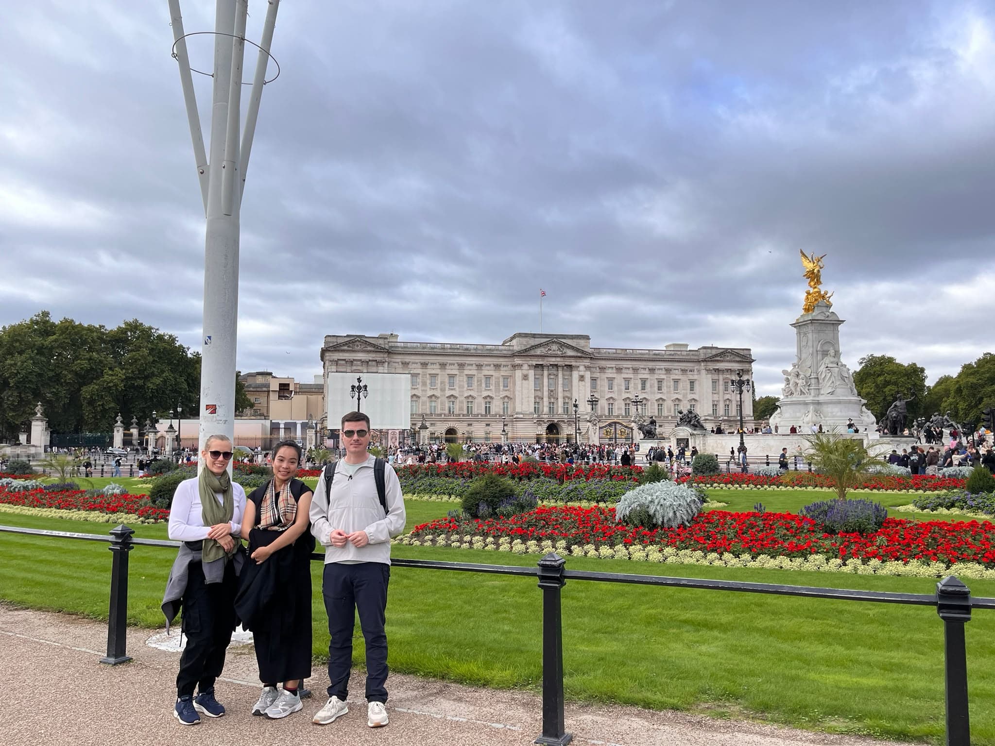 Two guests with their guide beside the flowerbeds in front of Buckingham Palace