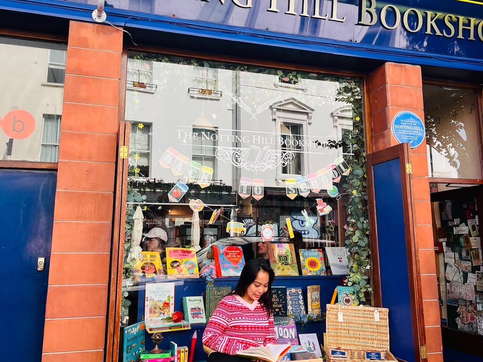 The BeExplorers guide reading on the bench outside The Notting Hill Bookshop's blue shopfront