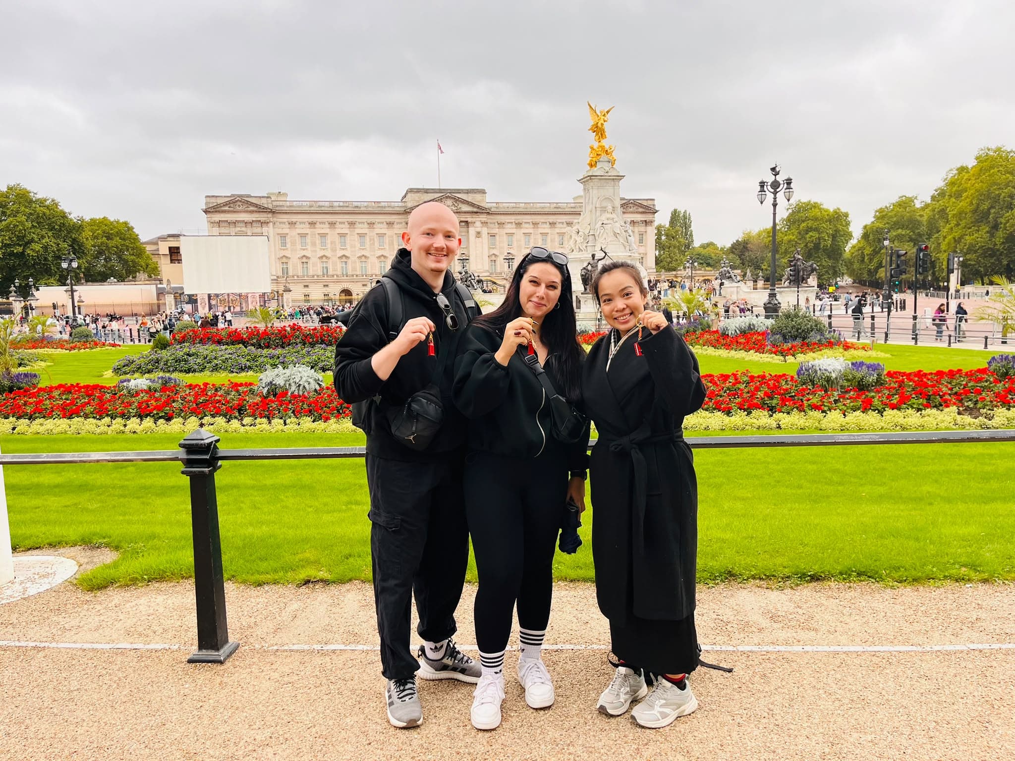 Three guests holding up their BeExplorers keyring souvenirs outside Buckingham Palace