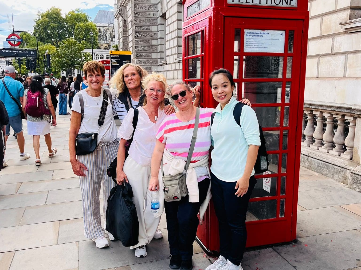 A BeExplorers group outside a red telephone box by Westminster station, with the Underground roundel and Westminster Abbey behind
